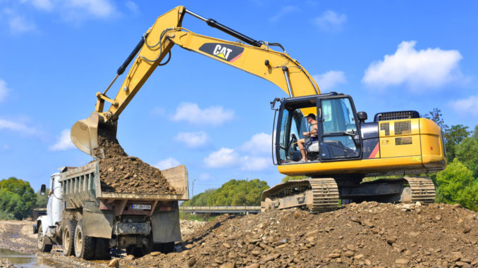 Excavator compacting earthfill embankment construction site